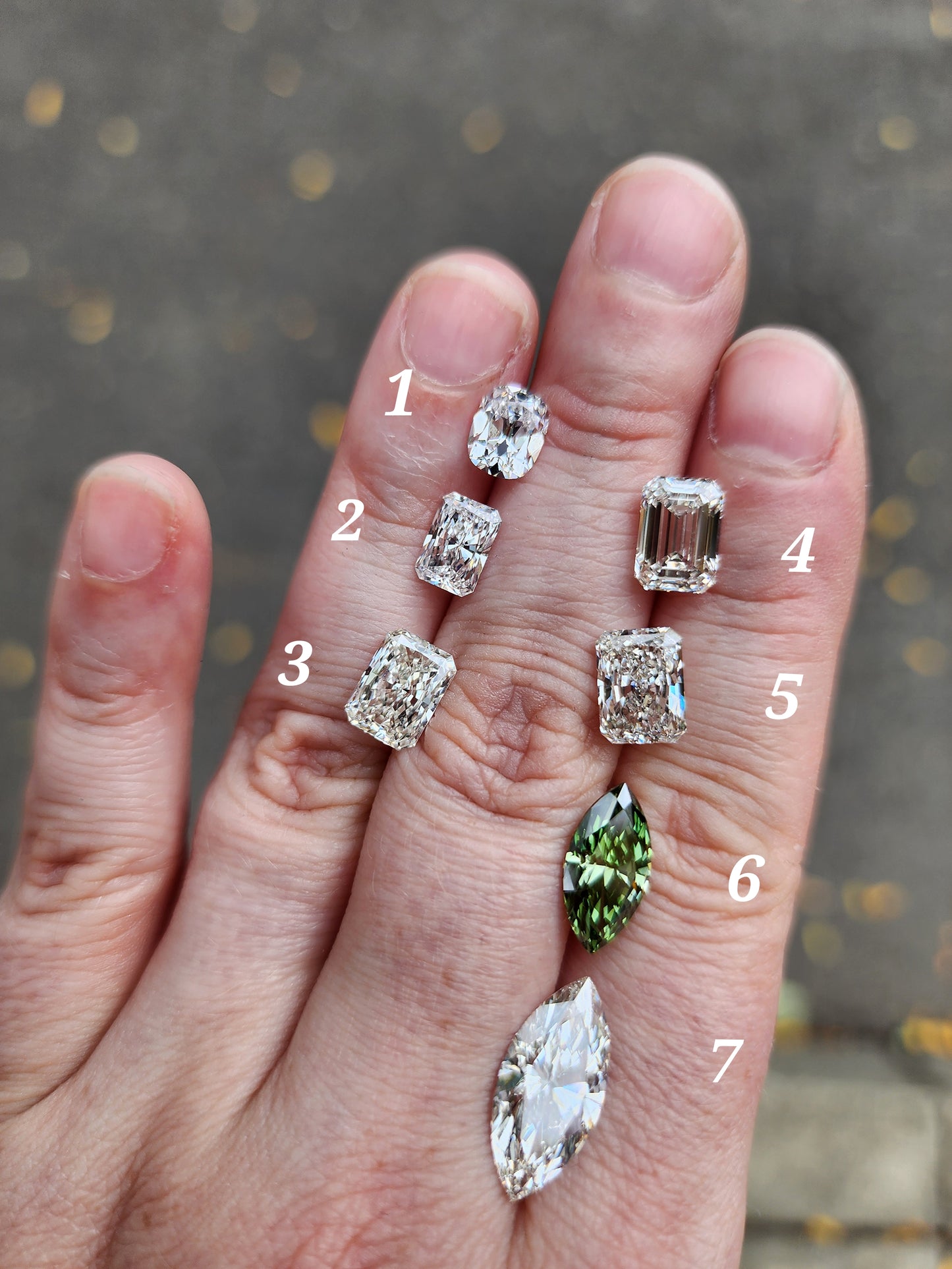 Hand displaying various cut and color diamond stones on a blurred background