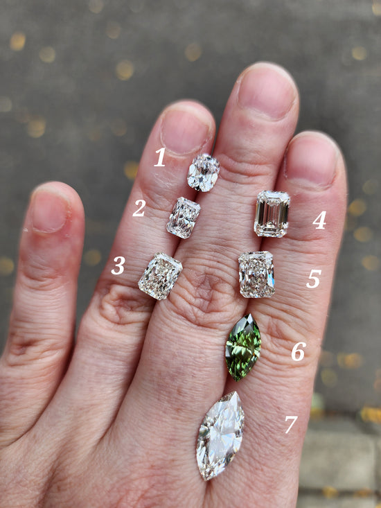 Hand displaying various cut and color diamond stones on a blurred background