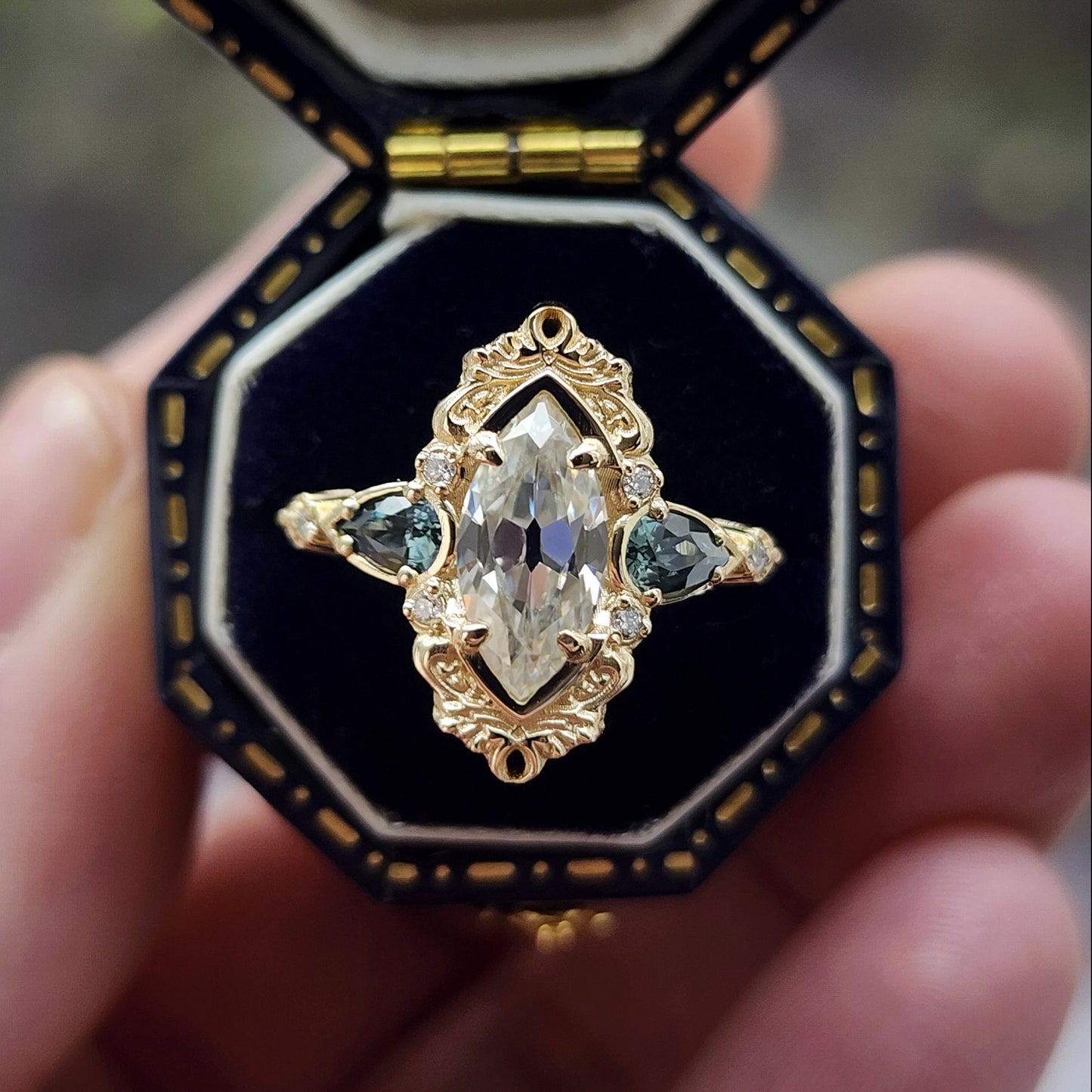 This Odette ring is a stunning piece, centered around a striking 1.20ct Moissanite Marquise, featuring an Old Mine Cut This center stone is beautifully complemented by Natural Australian Pear Sapphires, totaling .43ct, and accented with .05ct VS natural white diamonds Crafted in 14kt yellow gold image 1