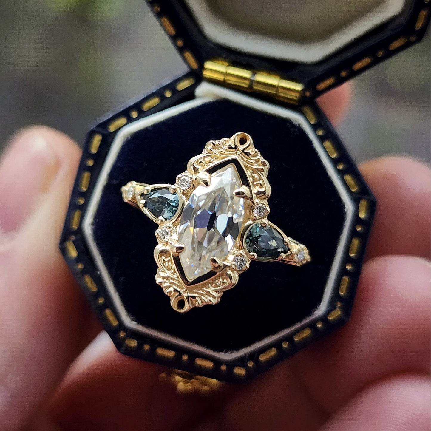 This Odette ring is a stunning piece, centered around a striking 1.20ct Moissanite Marquise, featuring an Old Mine Cut This center stone is beautifully complemented by Natural Australian Pear Sapphires, totaling .43ct, and accented with .05ct VS natural white diamonds Crafted in 14kt yellow gold image 3