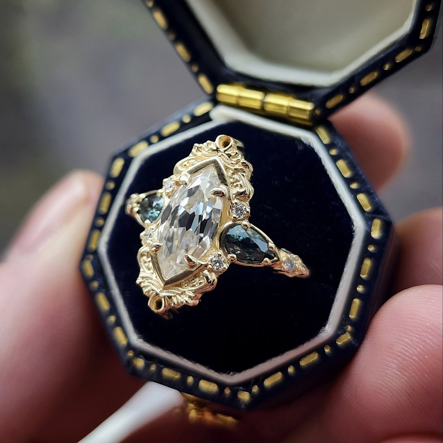 This Odette ring is a stunning piece, centered around a striking 1.20ct Moissanite Marquise, featuring an Old Mine Cut This center stone is beautifully complemented by Natural Australian Pear Sapphires, totaling .43ct, and accented with .05ct VS natural white diamonds Crafted in 14kt yellow gold image 5