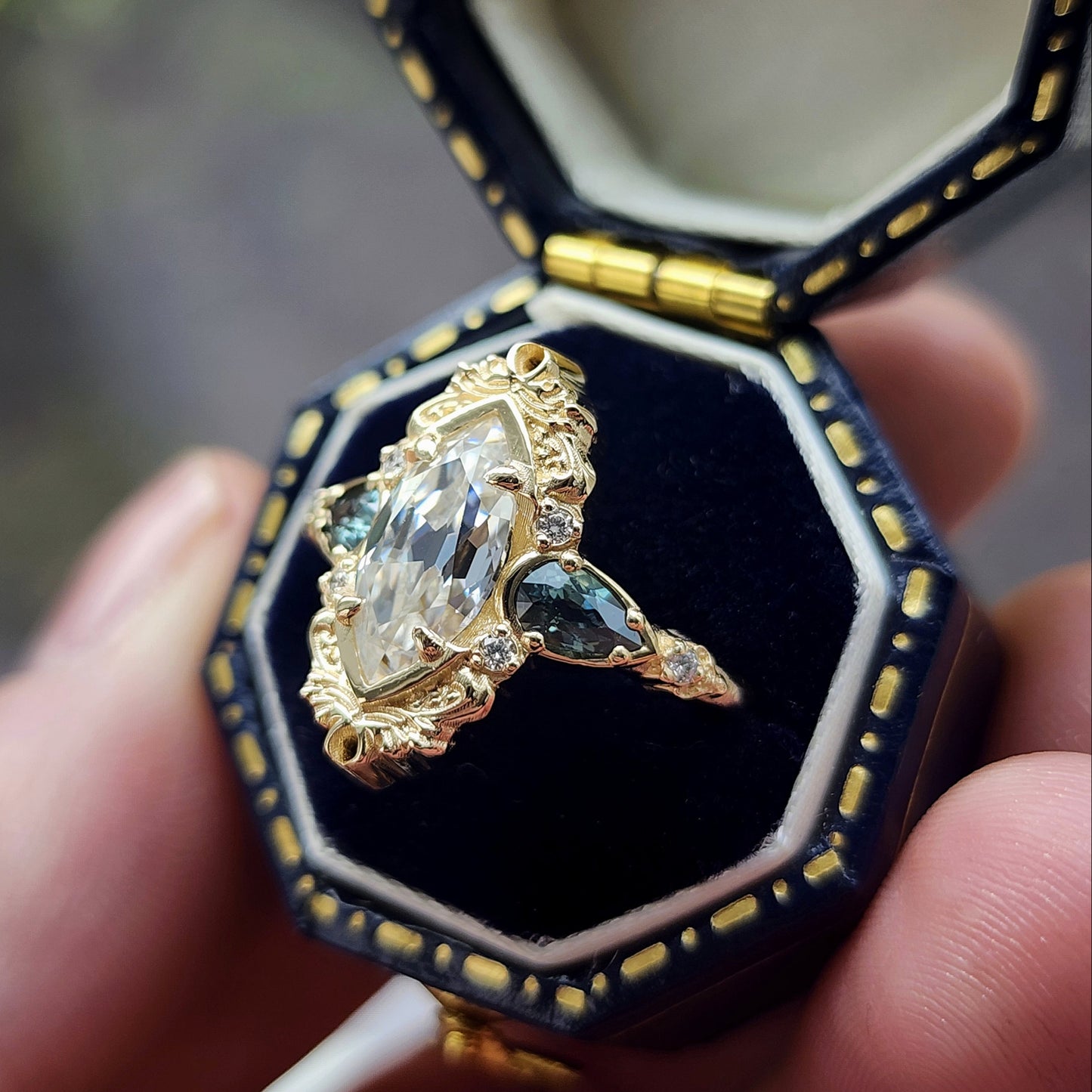 This Odette ring is a stunning piece, centered around a striking 1.20ct Moissanite Marquise, featuring an Old Mine Cut This center stone is beautifully complemented by Natural Australian Pear Sapphires, totaling .43ct, and accented with .05ct VS natural white diamonds Crafted in 14kt yellow gold image 7