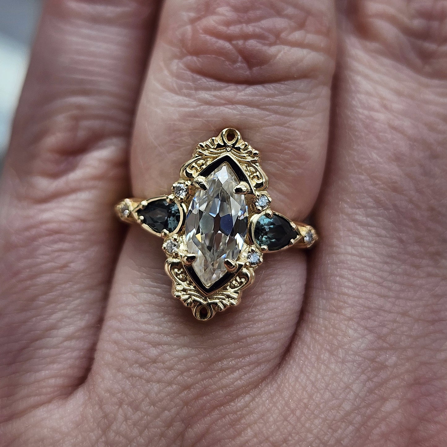 This Odette ring is a stunning piece, centered around a striking 1.20ct Moissanite Marquise, featuring an Old Mine Cut This center stone is beautifully complemented by Natural Australian Pear Sapphires, totaling .43ct, and accented with .05ct VS natural white diamonds Crafted in 14kt yellow gold image 8
