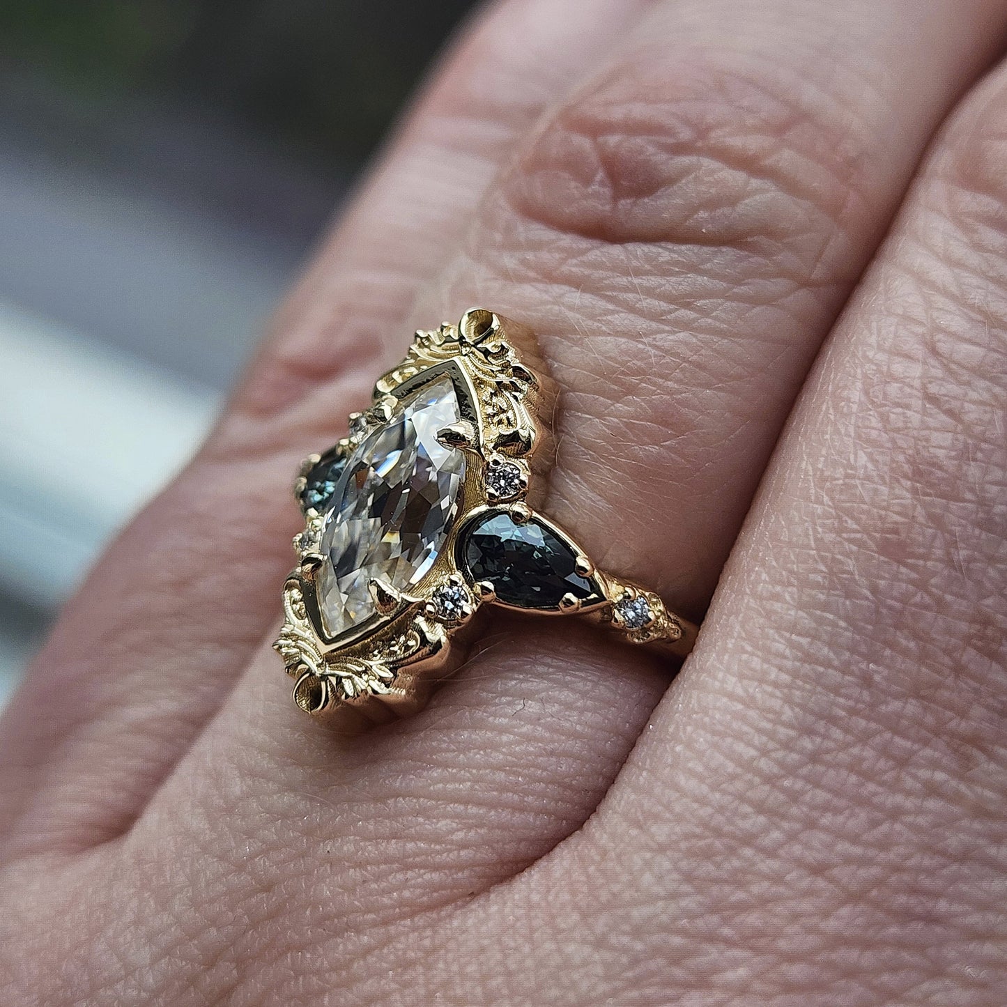 This Odette ring is a stunning piece, centered around a striking 1.20ct Moissanite Marquise, featuring an Old Mine Cut This center stone is beautifully complemented by Natural Australian Pear Sapphires, totaling .43ct, and accented with .05ct VS natural white diamonds Crafted in 14kt yellow gold image 11