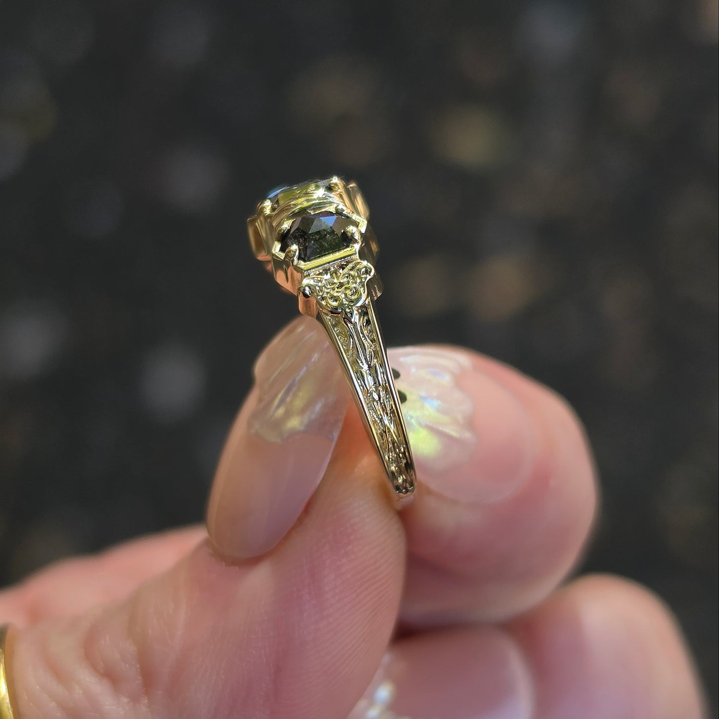 A close-up of a hand holding a yellow gold ring  set against a dark blurred background.