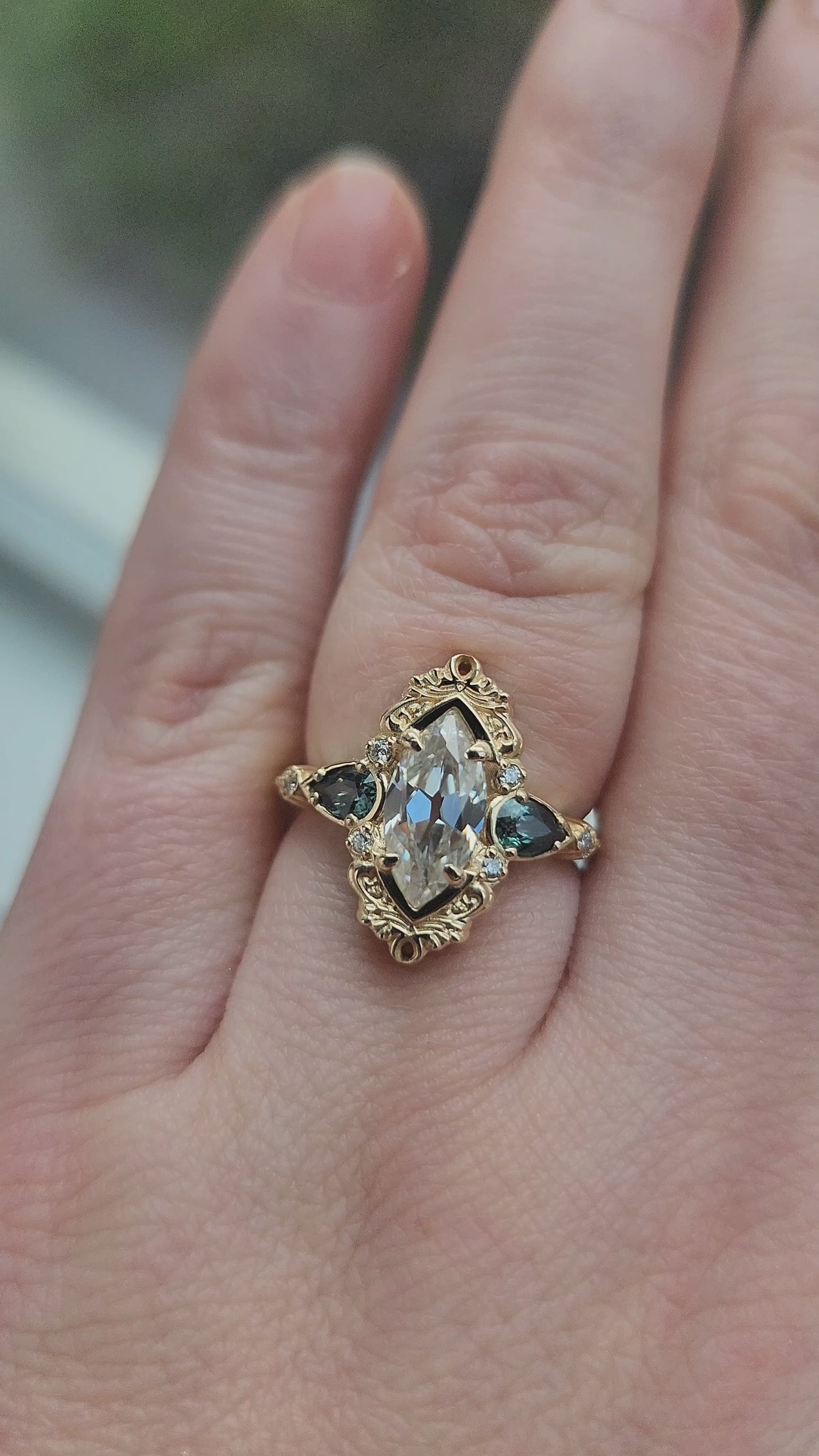 Load and play video in Gallery viewer, This Odette ring is a stunning piece, centered around a striking 1.20ct Moissanite Marquise, featuring an Old Mine Cut This center stone is beautifully complemented by Natural Australian Pear Sapphires, totaling .43ct, and accented with .05ct VS natural white diamonds Crafted in 14kt yellow gold video 1
